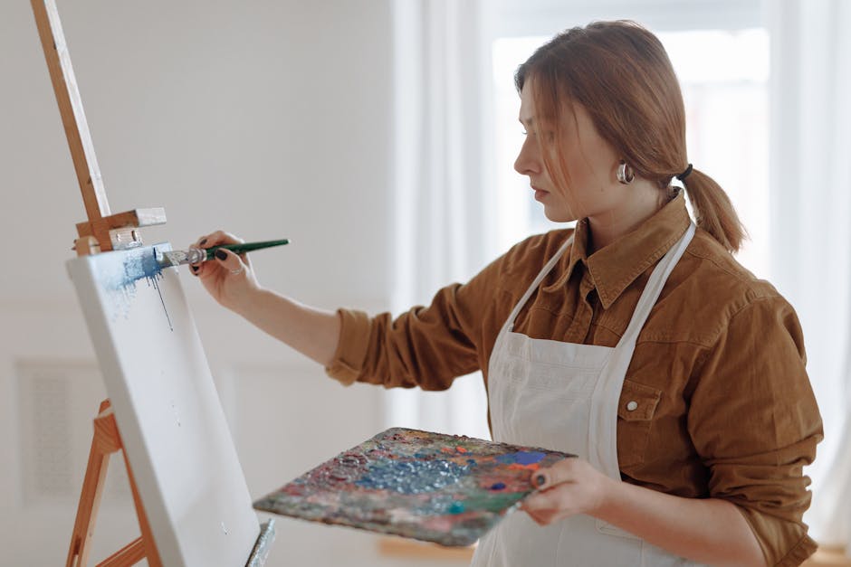 Woman artist painting on a canvas with a brush in a bright indoor studio.