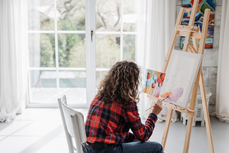 A person painting on a canvas in a bright, sunlit studio with large windows.